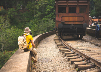 Traveler taking photo of vintage wooden train on the Nine Arches Bridge in Sri Lanka on his phone.