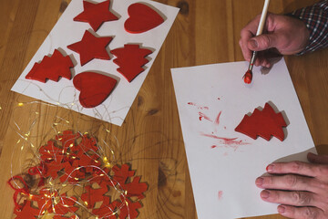 Painting red wooden christmas decorations for holiday crafting