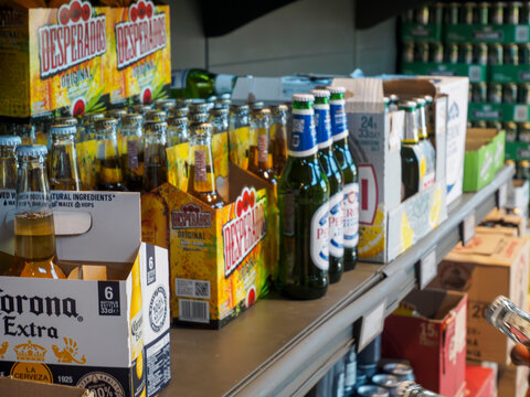 Rows of Corona Extra and Desperados beer bottles and cases on display shelves in a retail store with a customer reaching for a bottle