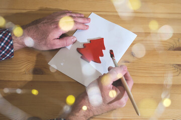 Hands painting red christmas tree shape on paper