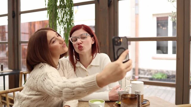 Two bloggers sit together making a duck face selfie for social media sharing a fun friendly moment relaxed atmosphere and casual connection while creating lighthearted content in a cozy cafe