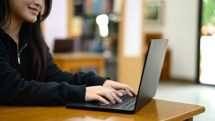 Cropped shot teenage asian woman education or internet encyclopedia concept. Open laptop in library