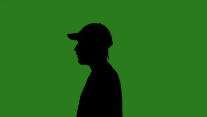 A black isolated silhouette of a man wearing a cap against a green chroma key background, side view. Minimalistic contrast and modern visual composition.