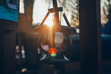 Hanging lantern silhouetted against bright, setting sun flare. Decorative lantern captured during golden hour