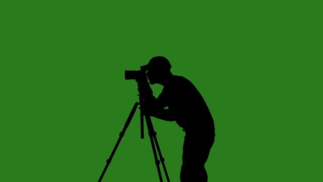 Black isolated silhouette of a male cameraman with a camera on a tripod against a green chroma key background. Minimalist contrast and modern visual composition, mockup.
