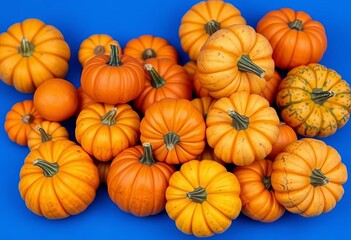 A cluster of various-sized pumpkins, some showing orange and green hues, rests on a smooth, vibrant blue background ,  photography,  pumpkins on blue