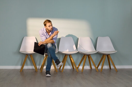 Man waiting for interview in office corridor. The job candidate sits on a chair with a resume, rehearsing answers as anxiety grows in the quiet lobby. Concept: job interview waiting anxiety.