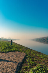 Peaceful river landscape with person walking near water and nature under bright blue sky view scenery