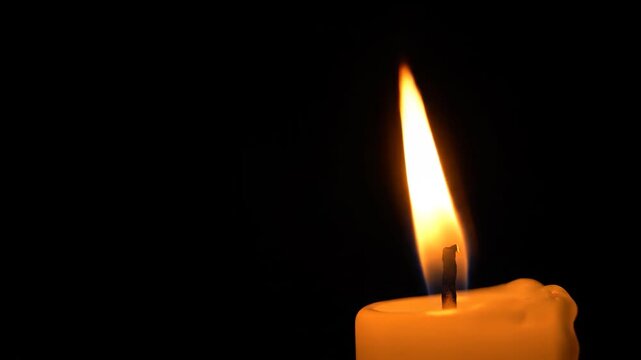 Single candle flame burning in darkness