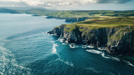 Obraz premium Aerial view of rugged sea cliffs and green patchwork farmland along the Atlantic coast of Ireland on a partly cloudy day. 