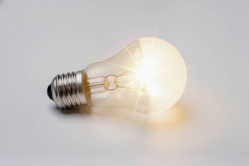 A burning incandescent light bulb lying horizontally on a smooth white-gray surface with a bright star effect visible.