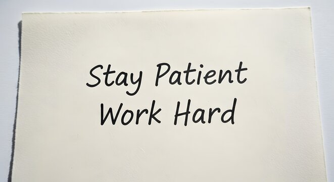 A motivational handwritten note on a white paper encouraging perseverance and dedication with the words 'Stay Patient Work Hard' in black ink