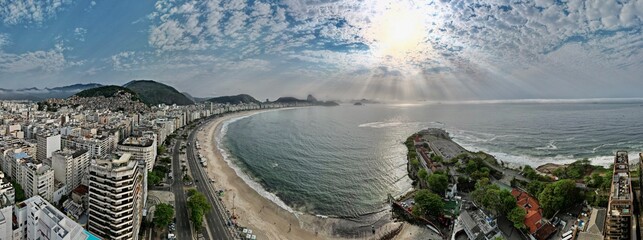 Panoramic aerial view of coastal city and curved beach under cloudy sky