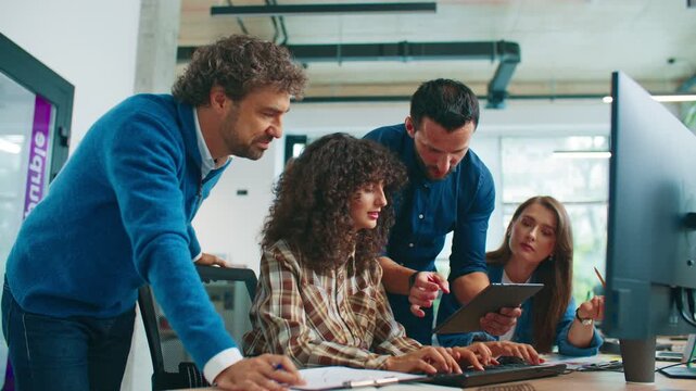 Male coworker holding tablet explaining project details to group gathered around desk. Team listening attentively and discussing strategy while working together in bright collaborative office.