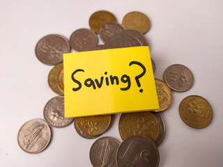 The image shows a yellow sticky note with the word Saving on it, placed on a pile of Malaysian coins
