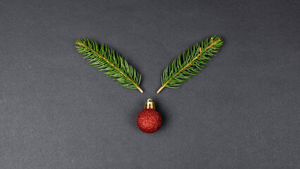 Reindeer concept made with fir branches and red Christmas ball decoration on black paper background
