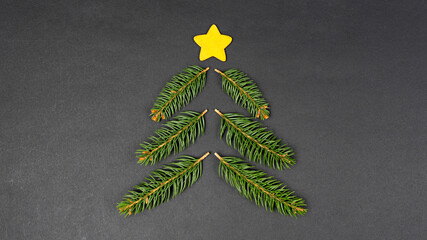 Christmas tree concept made with fir branches and yellow star decoration on black paper background