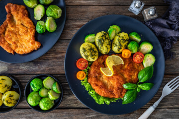 Crispy breaded chicken cutlet with boiled potatoes and Brussels sprouts on wooden table. Top view