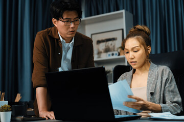 Serious face of thinking businesswoman project job with coworker to taking paperwork for checking with signed business plan for company stock market at over late night time at modern office. Infobahn.