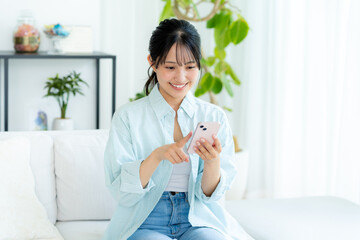 部屋でスマホを操作する若い女性