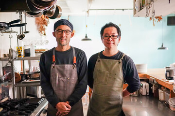 Portrait of two friendly chefs wearing aprons standing i