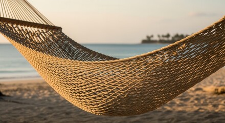 Obraz premium Close-up of an empty rope hammock on a sandy beach at sunset. Tropical vacation background with a view of the ocean and a distant island