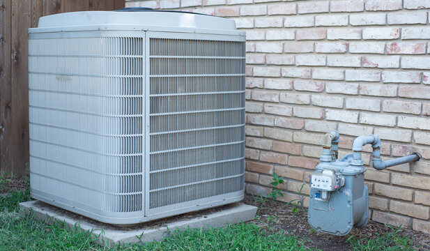 Panorama view house side yard with central AC condenser and natural gas meter with regulator pipe, installed on concrete pads near brick siding, grass lawn in Coppell, Texas residential zone