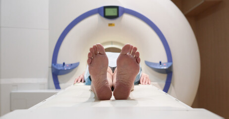 Unrecognizable female patient lying barefoot on bed of modern MRI machine before going through scan