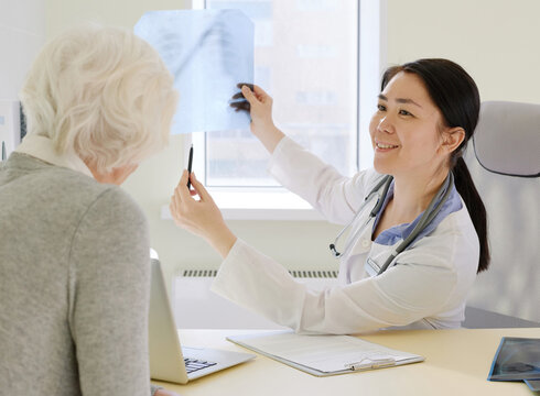 Female physician discussing positive results of MRI examination with female senior patient, showing her radiograph and smiling