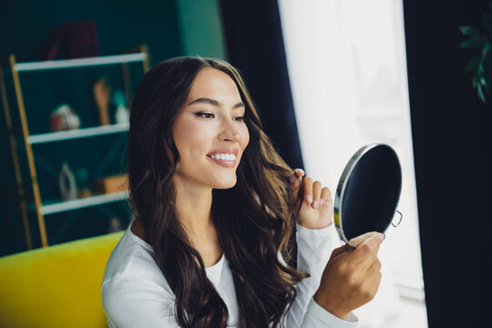 Young woman smiles while checking her reflection in a round mirror in a bright home interior with a couch and bookshelf in a cozy living room