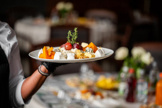 Elegant cheese platter with assorted cheeses, grapes, and nuts presented by a gloved waiter at a catered event or restaurant