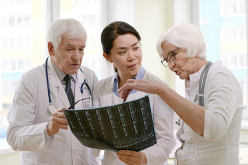 Group of experienced male and female doctors examining X-ray of patient after MRI test in hospital, analysing results and discussing treatment