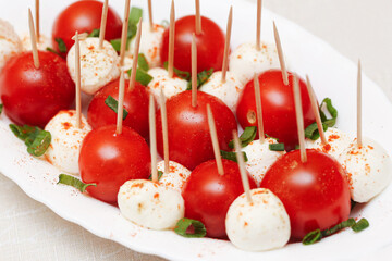 Tomato and mozzarella cheese skewers with herbs on white plate. Fresh appetizer sticks with basil...