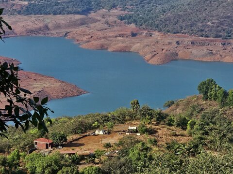 Hilltop lake and village Aerial view of a small village near a blue lake surrounded by green hills and dry terrain, depicting rural life and nature harmony. - Powered by Adobe