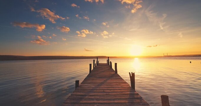 Golden Sunrise with Scenic Cloudscape Over The Lake and Wooden Pier and Calm Ripple water with Sun Reflections on the surface at Dusk