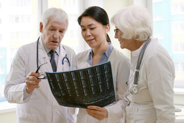 Group of professional male and female physicians looking at radiograph of patient after MRI scan, analyzing conditions and discussing further treatment