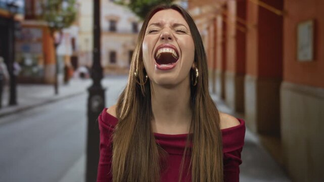 Young hispanic woman screaming with open mouth and raised eyebrows on a crowded city street in daylight; frustration.