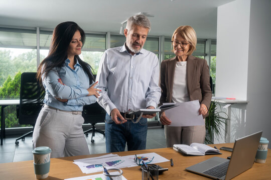 Diverse businesspeople Three busy happy middle aged professional business man and two women executive leaders team using laptop working on computer at work desk having conversation on financial projec