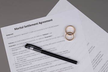 Marital Settlement Agreement paper document with wedding rings on table, ready for signature, symbolizing divorce, prenuptial contract, breakup, and separation.