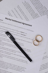 Marital Settlement Agreement paper document with wedding rings on table, ready for signature, symbolizing divorce, prenuptial contract, breakup, and separation.
