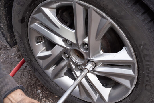 Close-up view of mechanic hands using wrench to tighten bolts on car wheel. Automotive service, maintenance and repair concept in detail.