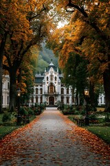 Naklejka premium Symmetrical photograph looking down a long path covered in vibrant red and yellow autumn leaves. This scenic path leads directly to a majestic palace framed by green trees.