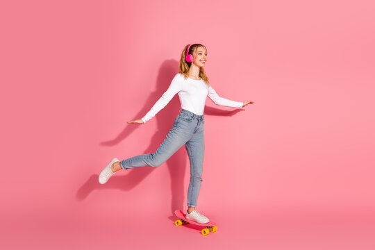 Happy young girl skateboarding indoors wearing casual style on pink background embracing joyful moments