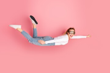 Young woman wearing goggles posing happily in flight pose with pink background showcasing energy...