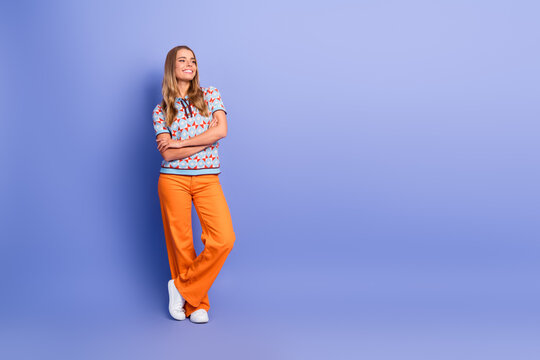 Young woman in bold orange pants and patterned top smiles while leaning against a blue wall showcasing casual fashion and a cheerful lifestyle
