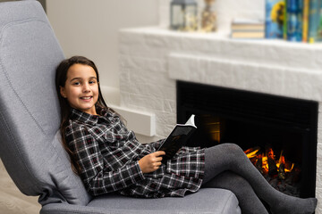little cute girl sitting n and reading book. Cozy interior