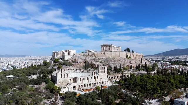 Dynamic low aerial zoom-out from the Parthenon and Herodion, revealing the Acropolis hill and its lush green natural surroundings.
