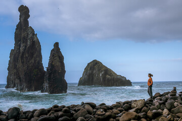 Traveler standing on rocky shore admiring sea stacks at Ribeira da Janela, Madeira Island, Portugal