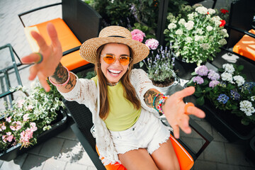 Happy traveler at a sunny terrace reaches out with a bright smile surrounded by colorful flowers in a vibrant garden setting