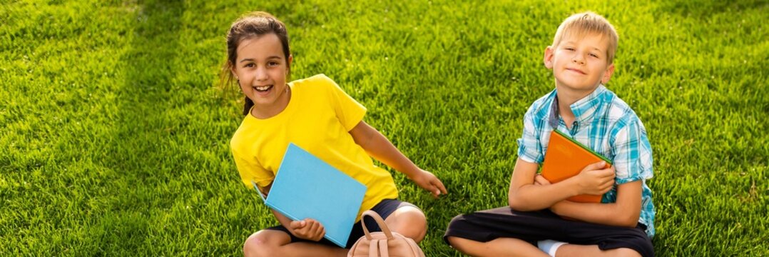Happy child sitting on the field holding tablet. Boy sitting on the grass on sunny day. Home schooling or playing a tablet